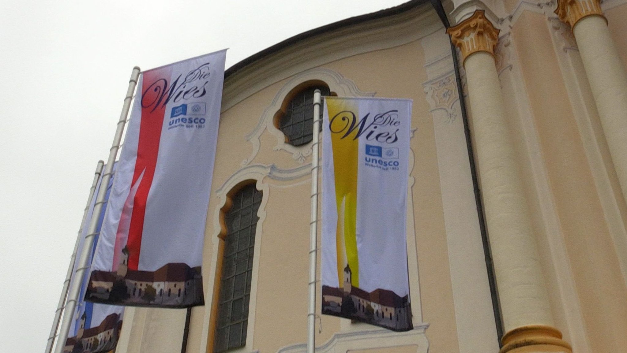 Zwei Flaggen vor der Wieskirche mit dem UNESCO–Emblem