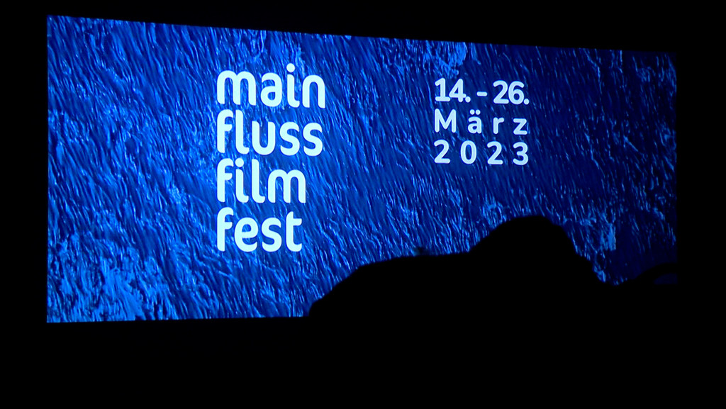 Blick auf die Kinoleinwand, auf der Main Fluss Film Fest 14.-26. März 2023 zu lesen ist. 