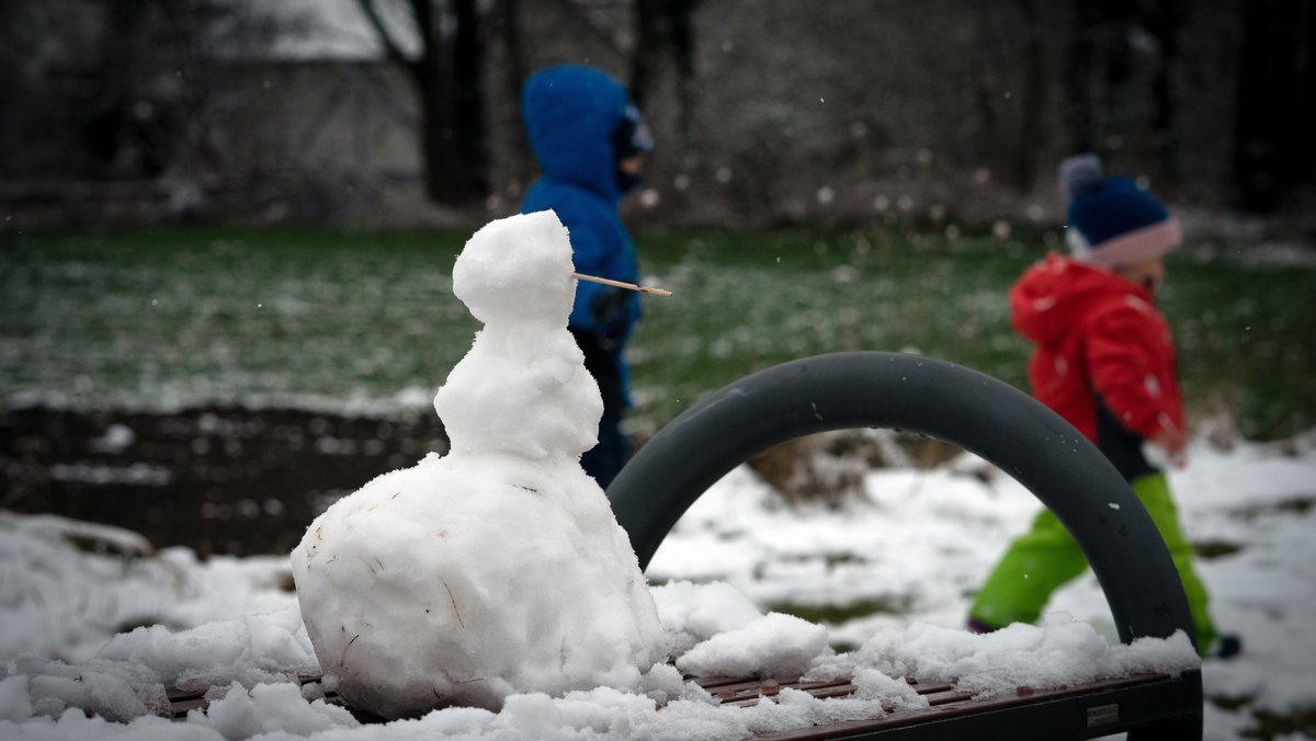Kinder gehen an einem kleinen Schneemann vorbei.