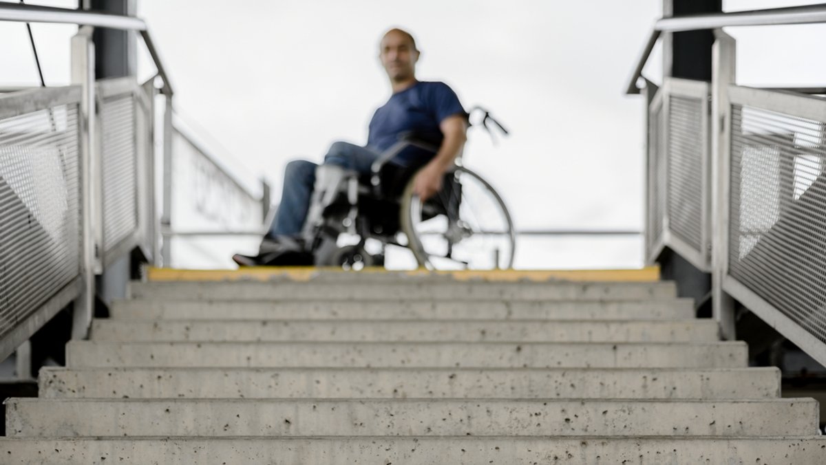 Symbolbild: Ein Mann im Rollstuhl vor einer Treppe. Bayern hat sein Ziel, im Jahr 2023 barrierefrei zu sein, nicht erreicht.