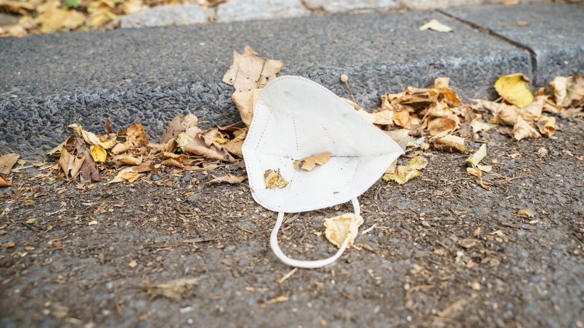 Eine FFP-2-Maske liegt am Straßenrand inmitten von vertrockneten Blättern.