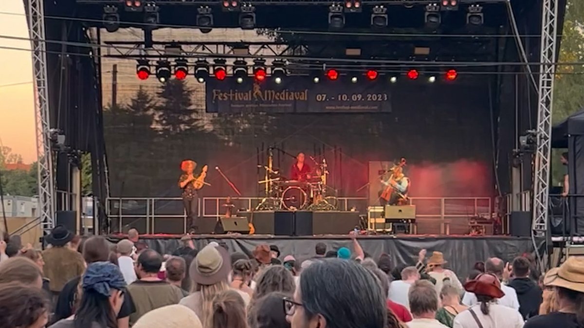 Eine Band mit drei Musikern auf der Bühne, davor stehen Zuschauer in Kostümen.