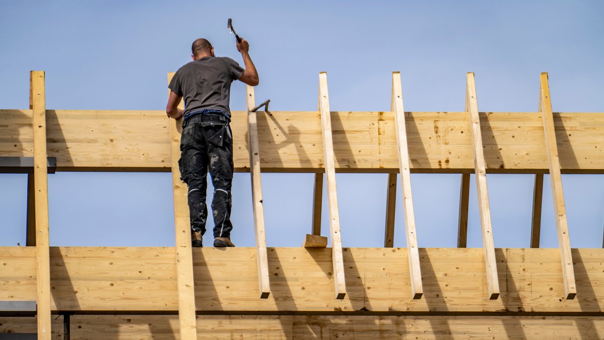 Ein Zimmermann arbeitet an einem Dachstuhl beim Neubau eines hölzernen Spitzdachs.