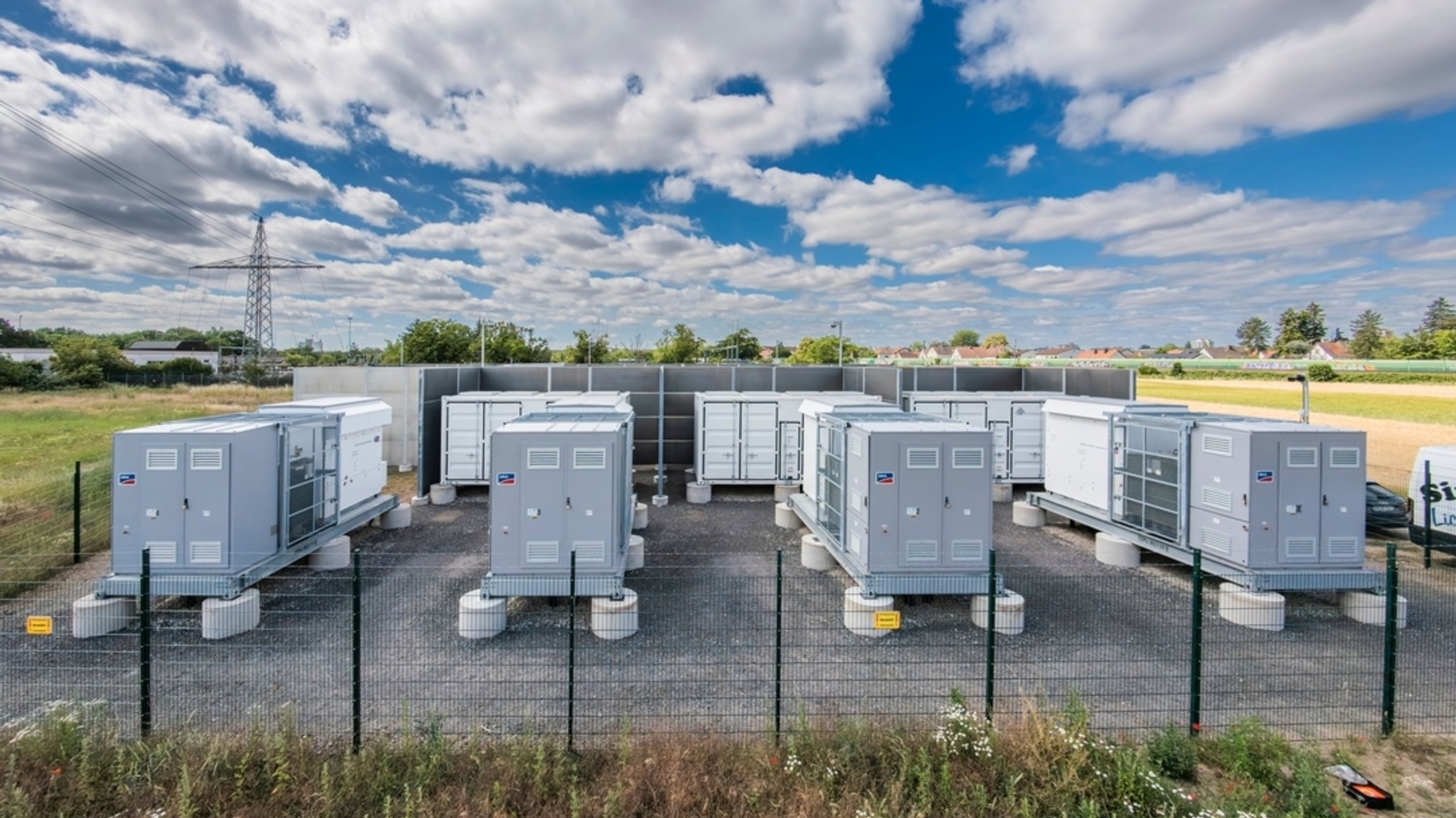 Container mit Batteriespeichern stehen auf einem eingezäunten und kameraüberwachten Areal.