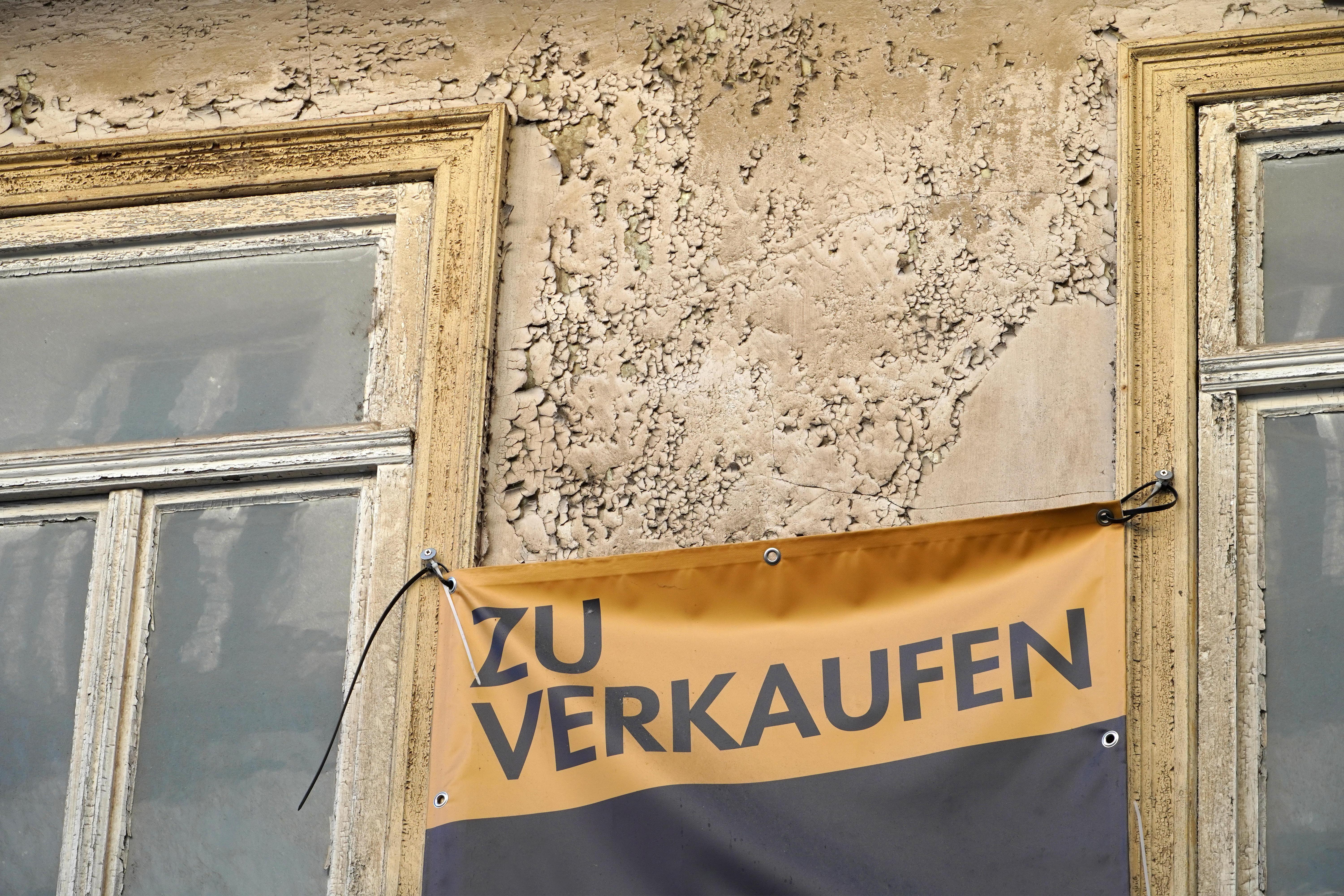 Plane mit Aufschrift "Zu verkaufen" an altem Wohnhaus
