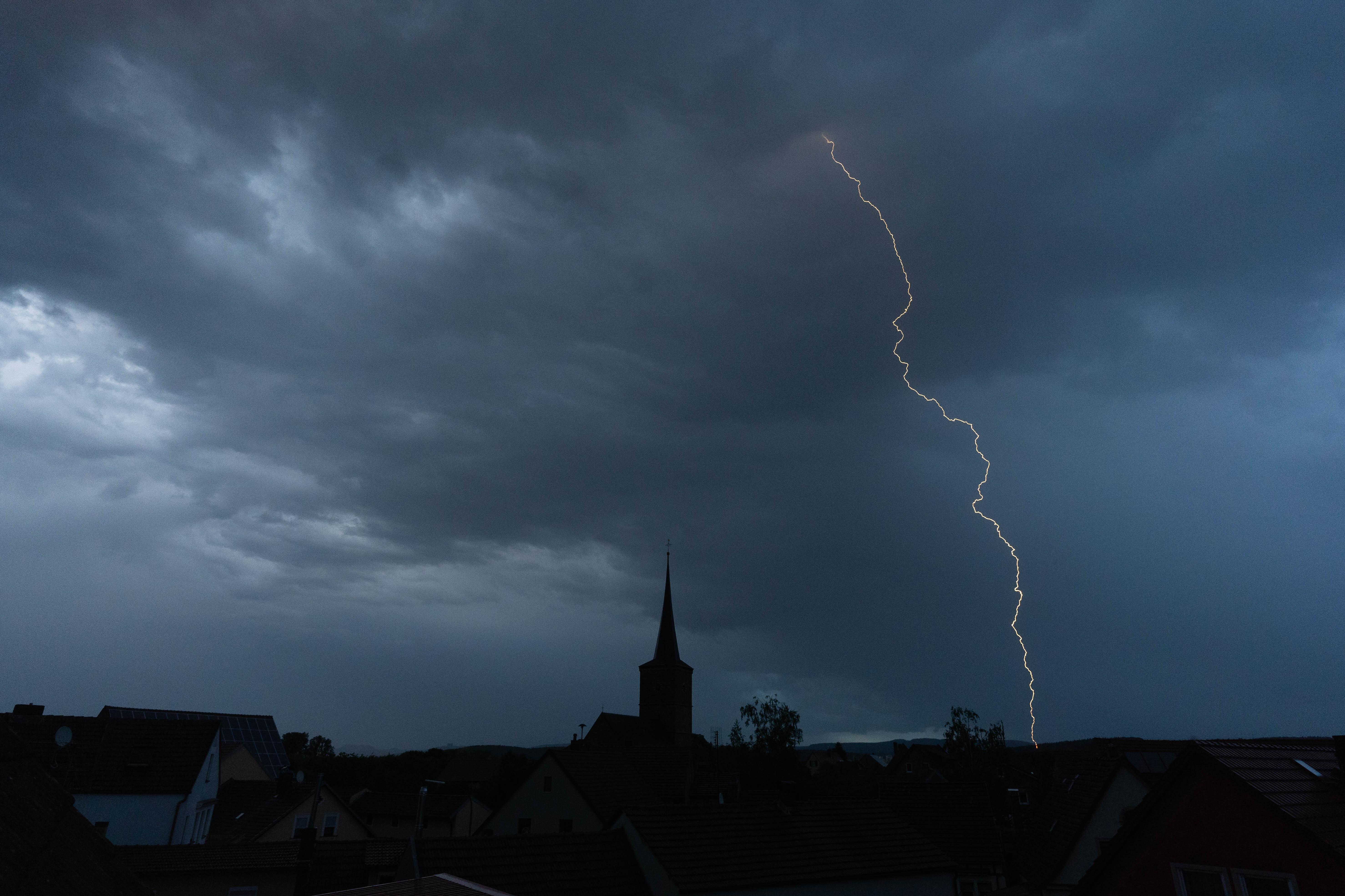 Blitze entladen sich aus einer Gewitterwolke über der Ortschaft.