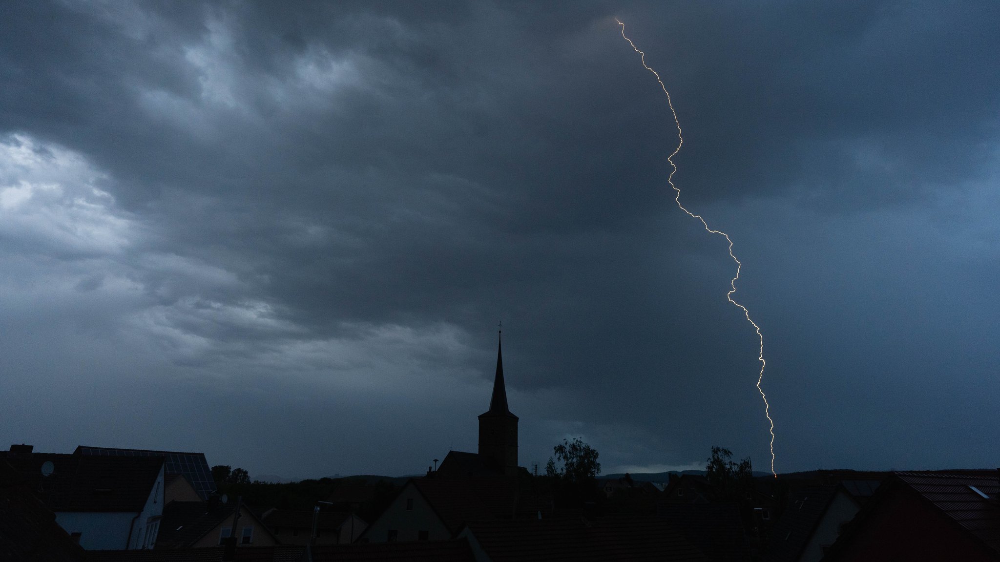 Blitze entladen sich aus einer Gewitterwolke über der Ortschaft.