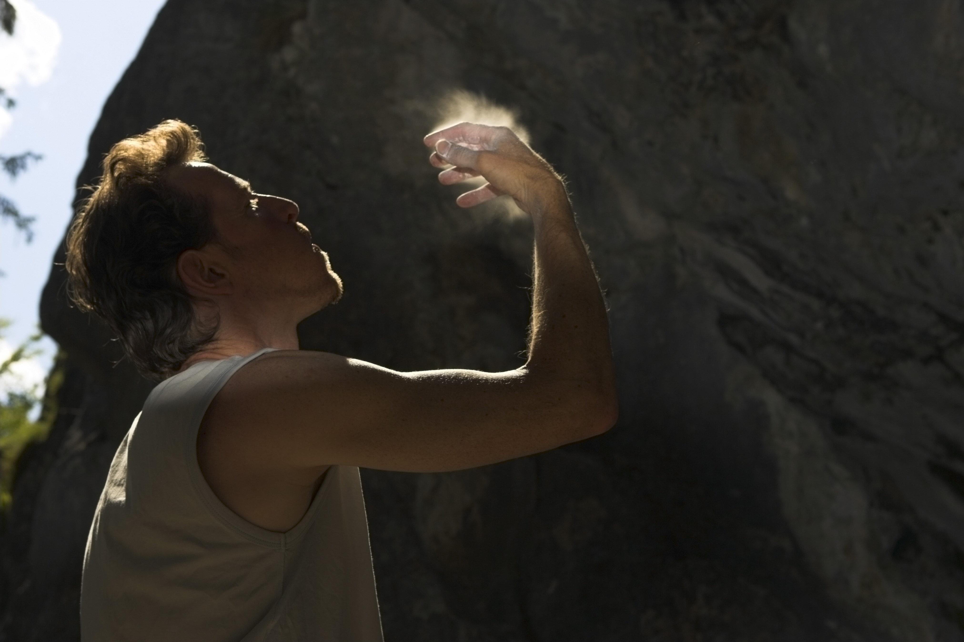 Ein Boulderer steht vor einer Wand und pustet sich Magnesia von der Hand.