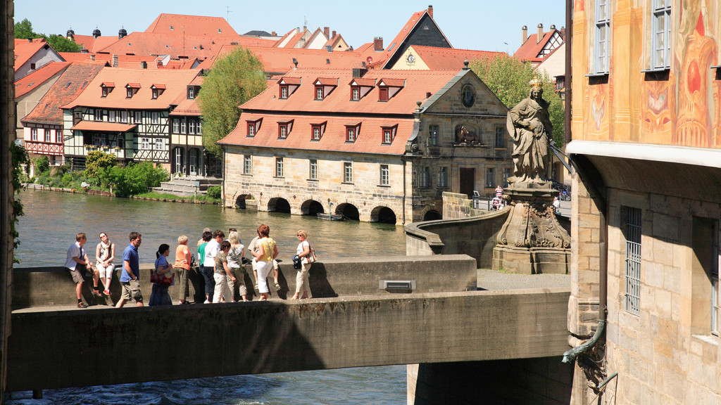 Mehrere Touristen stehen auf der Unteren Brücke in Bamberg und blicken über die Regnitz auf die Altstadt. 