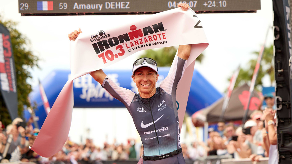 Eine strahlende Anne Haug hält die "Finishline" des Ironman 70.3 Lanzarote in die Höhe.