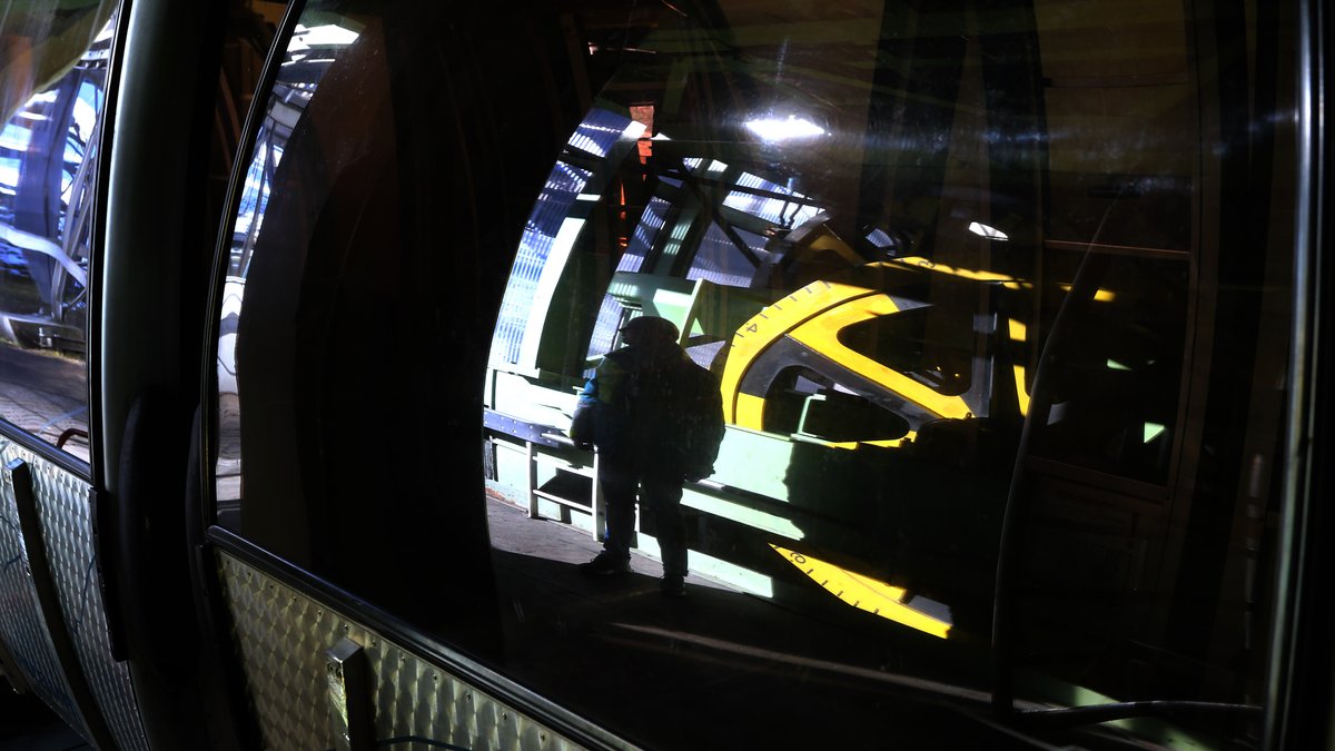 Ein Mann spiegelt sich neben einem Antriebsrad in der Talstation der Kanzelwandbahn im Fenster einer Gondel. 