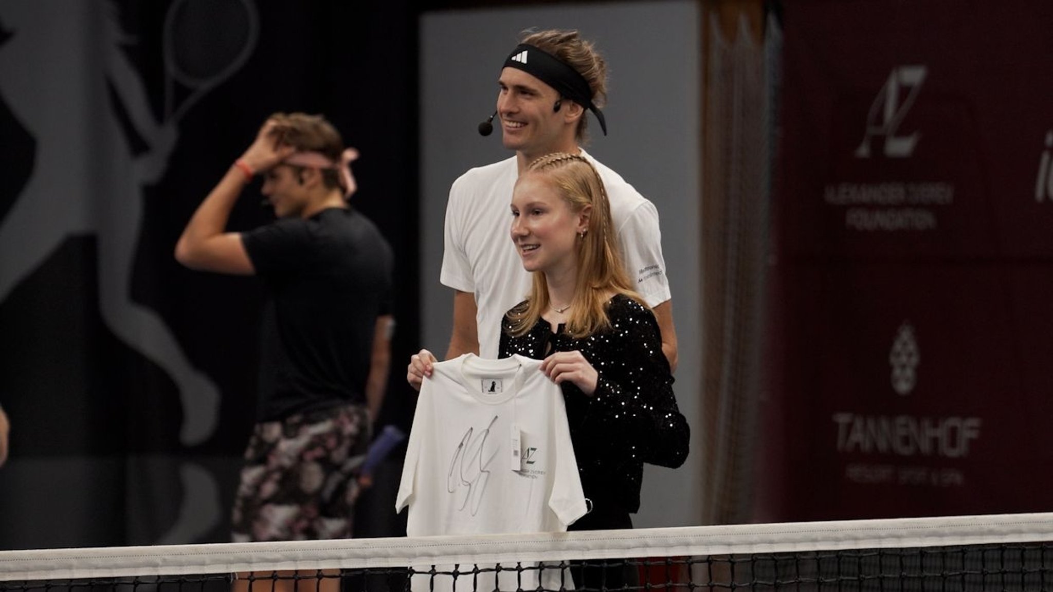 Zverev steht auf dem Tennisplatz und posiert mit einem jungen Fan für ein Foto.