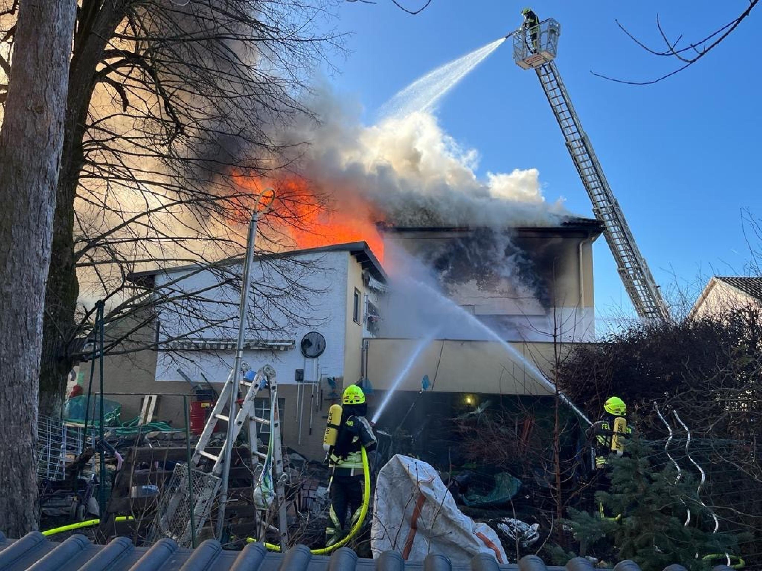 Feuerwehrleute spritzen von einer Drehleiter und vom Boden aus Wasser auf ein brennendes Gebäude