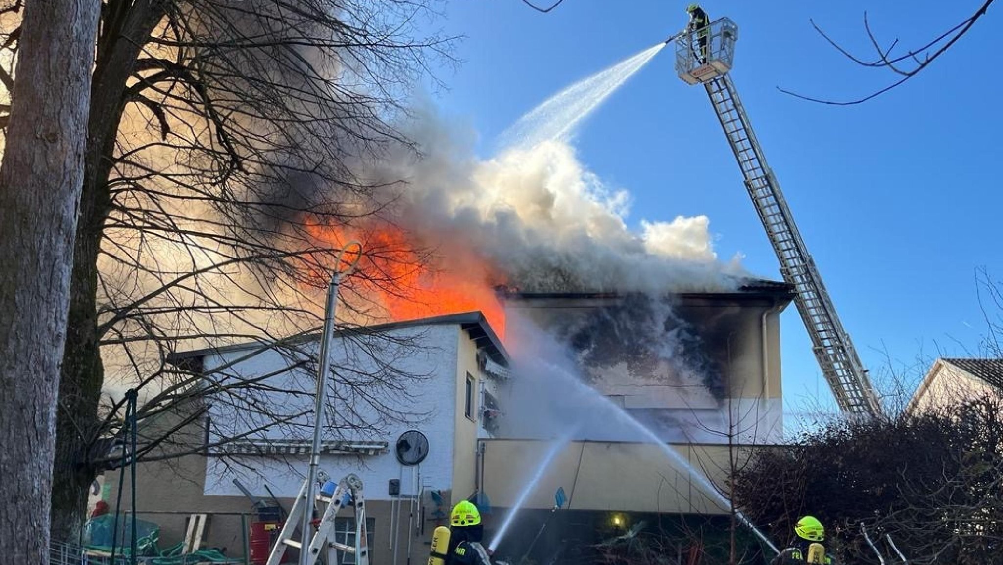 Feuerwehrleute spritzen von einer Drehleiter und vom Boden aus Wasser auf ein brennendes Gebäude