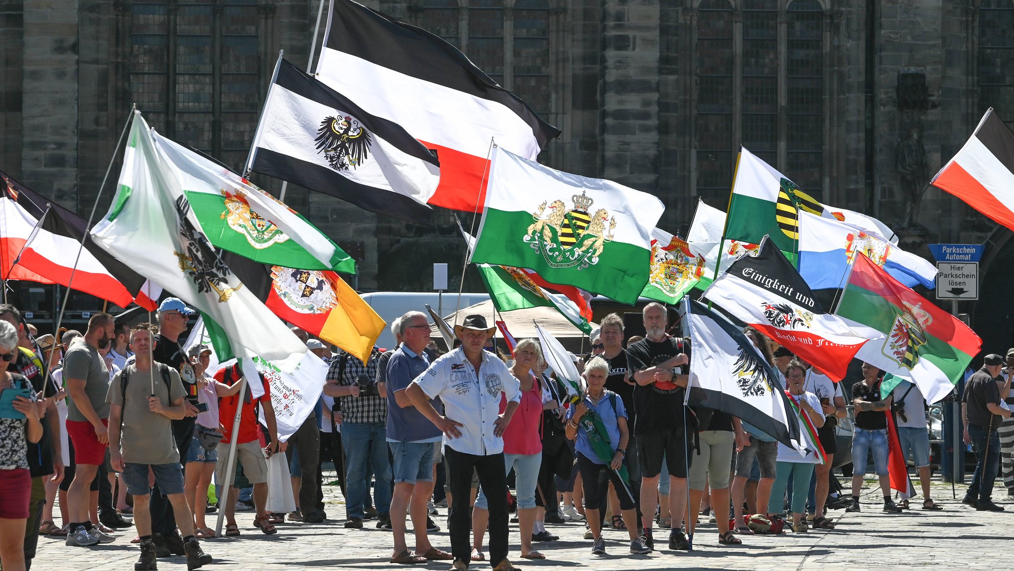 Archivbild: Reichsbürger-Demo in Magdeburg im August 2023. Reichsflaggen, Fahnen mit dem Reichsadler und Wappen verschiedener Herzogtümer und Königreiche werden von sogenannten Reichsbürgern bei der Demonstration auf dem Domplatz in die Luft gehalten.