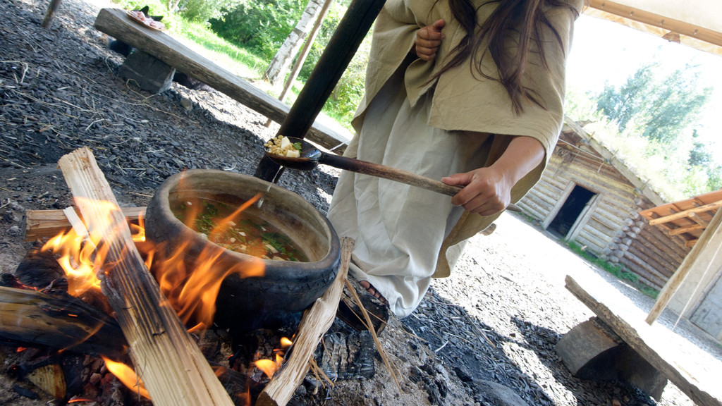 Frau nimmt essen aus Topf auf Feuer