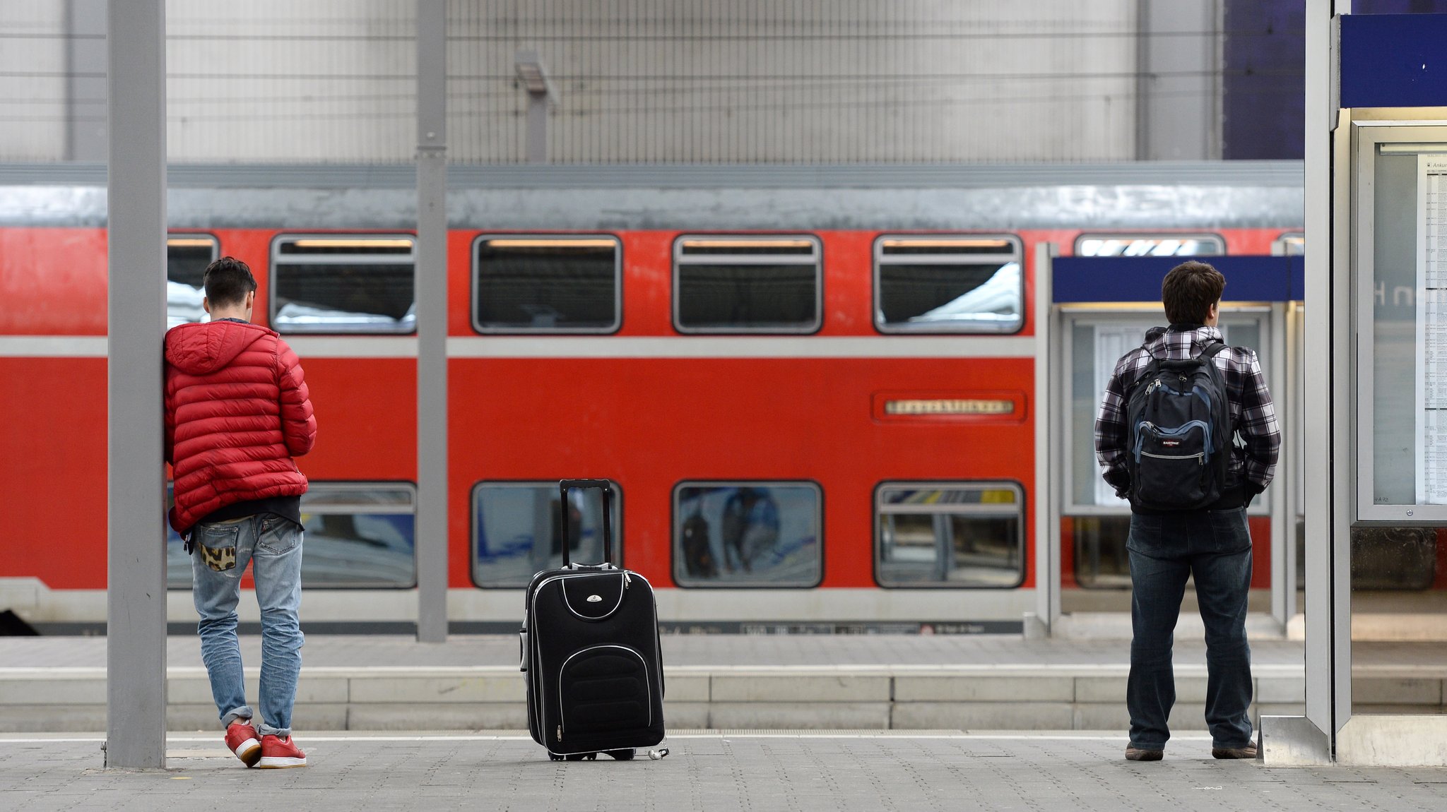 Zwei junge Männer warten an einem Bahnsteig im Hauptbahnhof in München (Bayern) auf einen Zug.