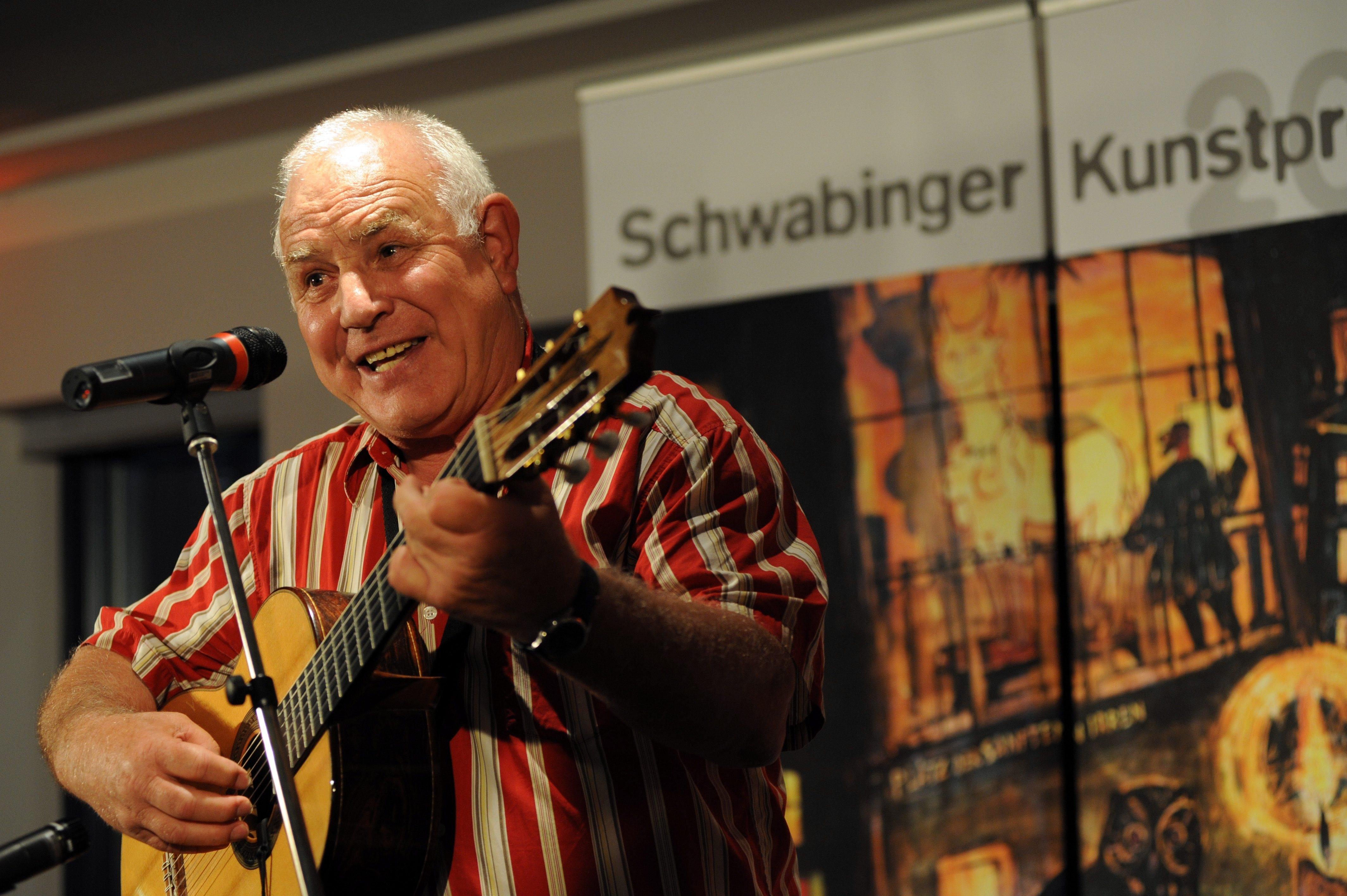 Ein Mann sitzt mit einer Gitarre vor einem Mikrofon.
