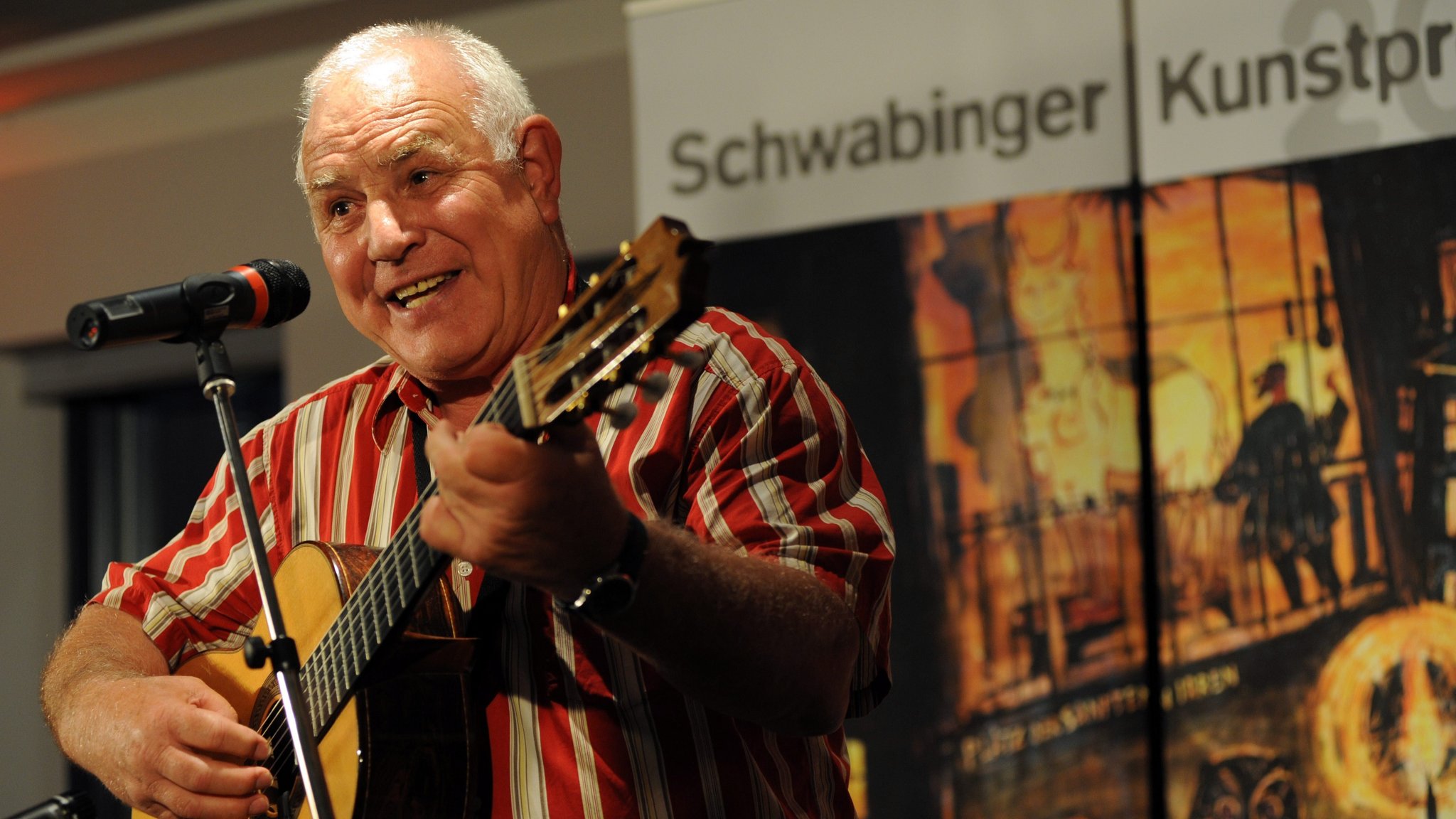 Ein Mann sitzt mit einer Gitarre vor einem Mikrofon.