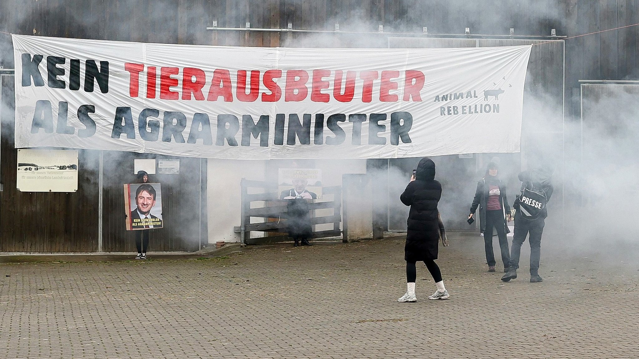 24.03.2025, Bayern, Lauf An Der Pegnitz: Mitglieder der Protestgruppierung Animal Rebellion halten Schilder mit Portraits vom Präsidenten des Bayerischen Bauernverbandes Felßner in die Höhe. Darüber ist ein Banner mit der Aufschrift „Kein Tierausbeuter als Agrarminister“ am Stall Felßners angebracht. | Bild: dpa-Bildfunk/--- 24.03.2025, Bayern, Lauf An Der Pegnitz: Mitglieder der Protestgruppierung Animal Rebellion halten Schilder mit Portraits vom Präsidenten des Bayerischen Bauernverbandes Felßner in die Höhe. Darüber ist ein Banner mit der Aufschrift „Kein Tierausbeuter als Agrarminister“ am Stall Felßners angebracht.