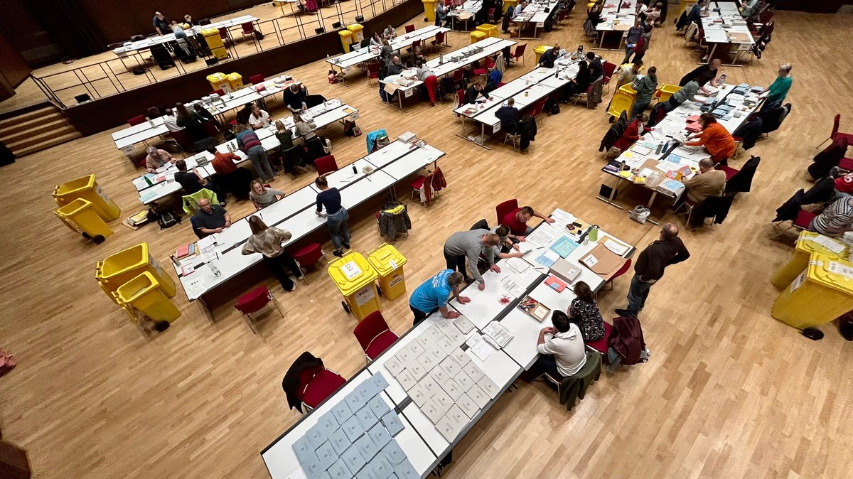 Tische mit Wahlunterlagen in einer großen Halle.