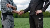 Zwei Personen in Arbeitskleidung stehen auf einem Getreidefeld und reichen sich die Hand (Symbolbild) | Bild:picture-alliance / Countrypixel | FRP