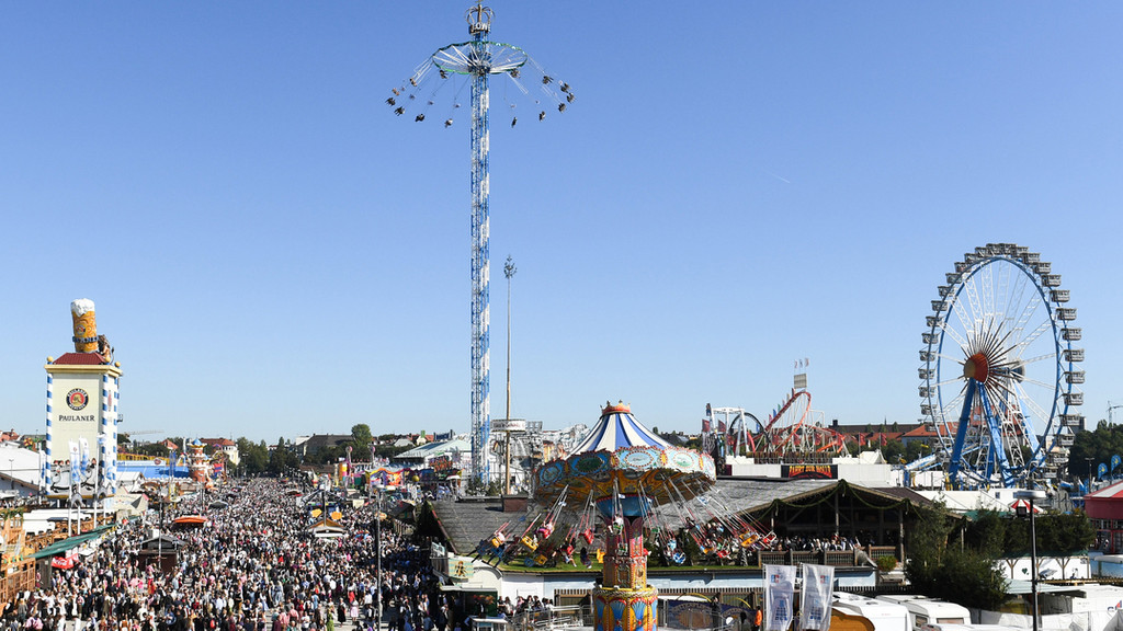 Blick auf die Theresienwiese, während das Oktoberfest stattfindet (aus dem Jahr 2019). Man sieht Fahrgeschäfte und sehr viele Besucherinnen und Besucher. 
