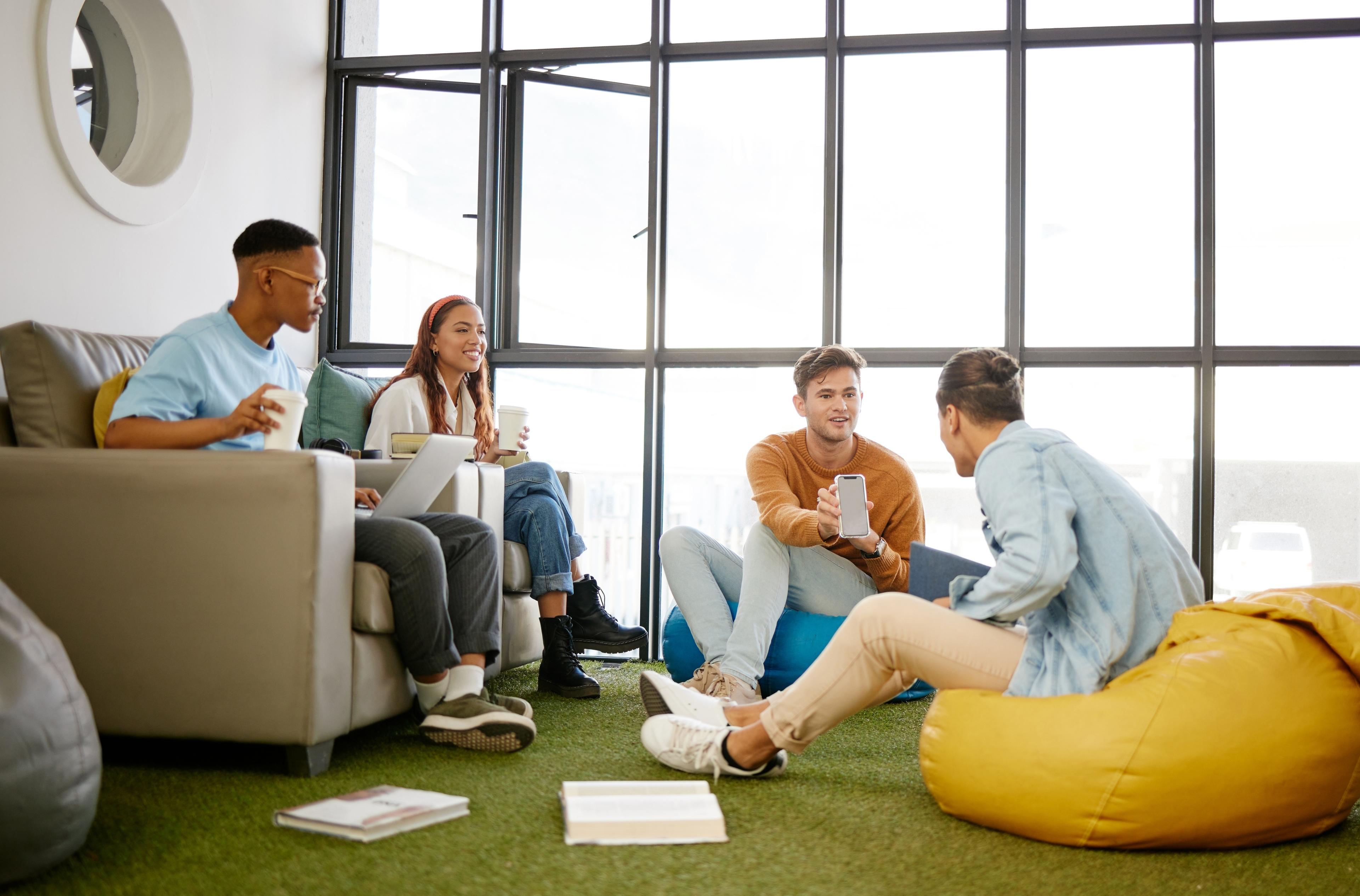 Lernen der Zukunft - so könnte es aussehen: Jugendliche auf Sitzkissen und Sofa mit Laptops und Smartphone beim Wissensaustausch.