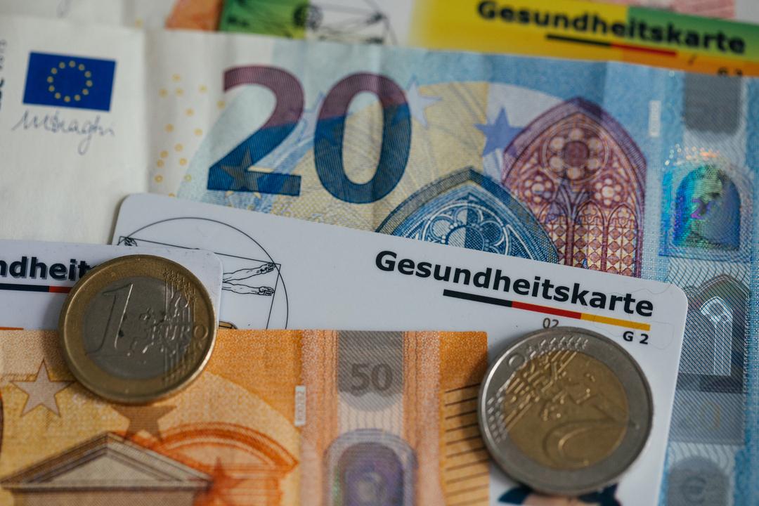 Geldscheine und Münzen, zwischen denen eine Kassen-Chipkarte liegt