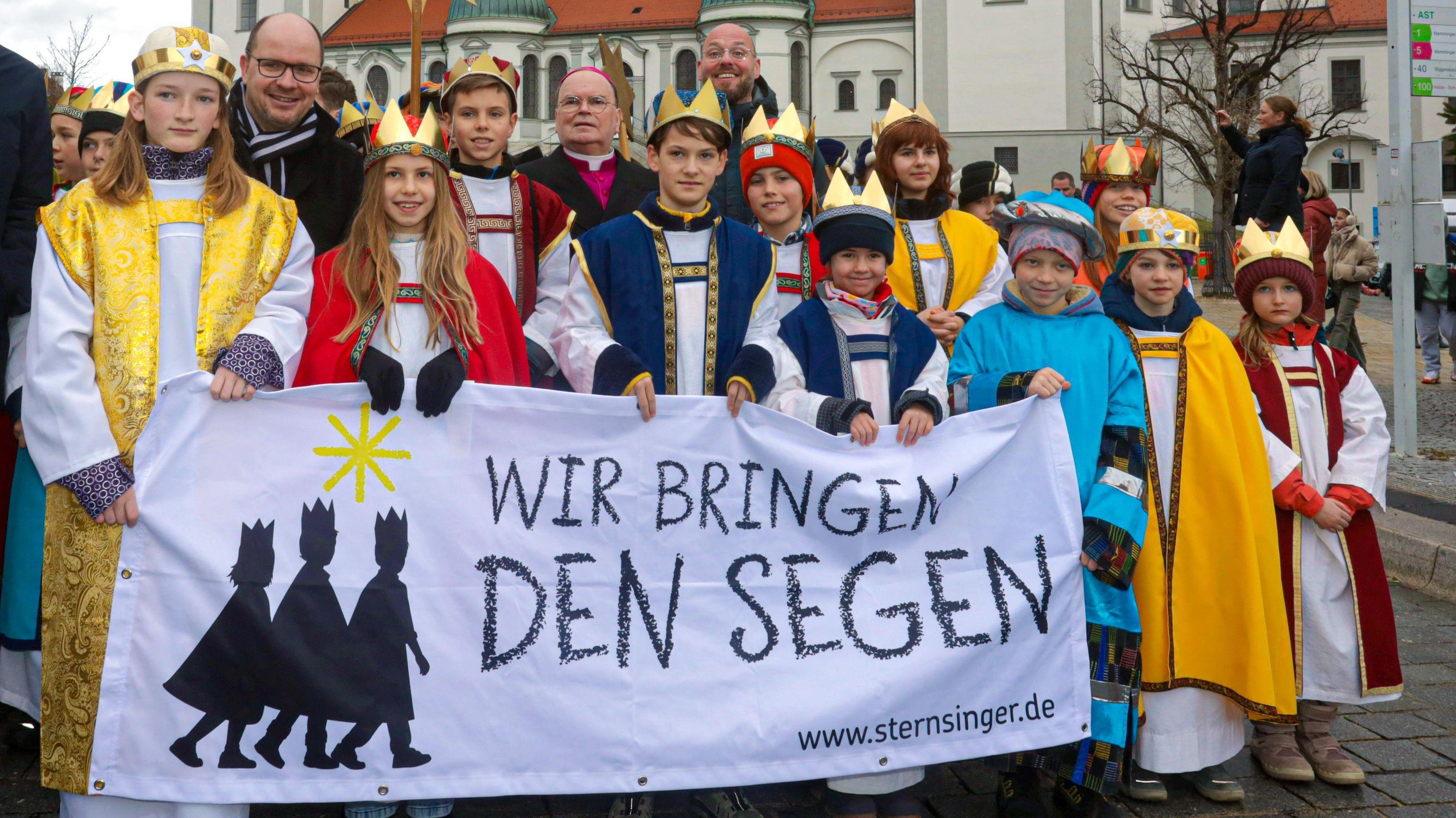 Sternsinger in Kempten. Sie tragen ein Transparent, auf dem "Wir bringen den Segen" steht.