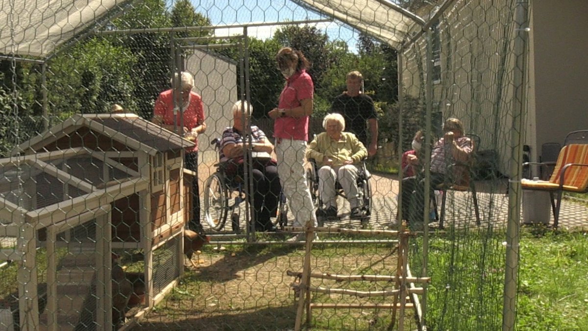Bewohnerinnen eines Harburger Pflegeheims sitzen vor einem Hühnerauslauf.