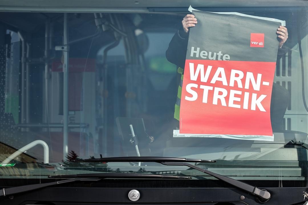 (Symbolbild) Ein Mitarbeiter befestigt während eines Warnstreiks ein Plakat in einem Bus auf einem Betriebshof.