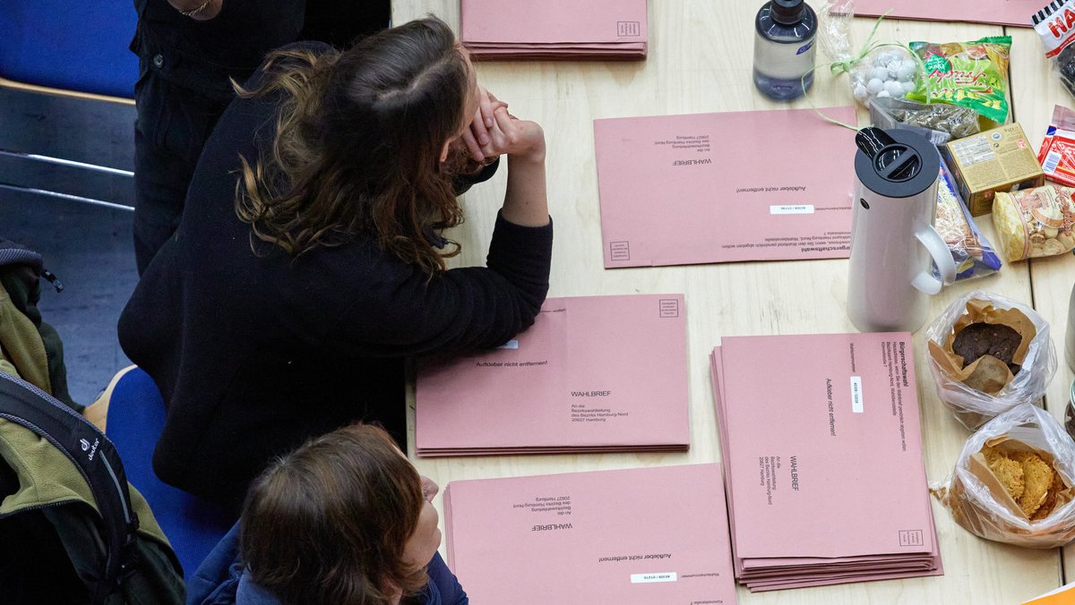 Wahlhelfer bei der Hamburger Bürgerschaftswahl. Auf dem Tisch liegen Stapel mit Wahlbriefkuverts.