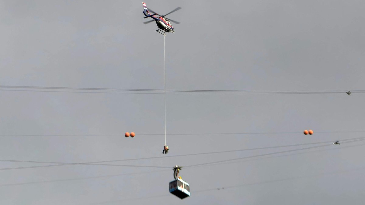 Ein Helikopter seilt Rettungskräfte zur feststeckenden Seilbahngondel ab.
