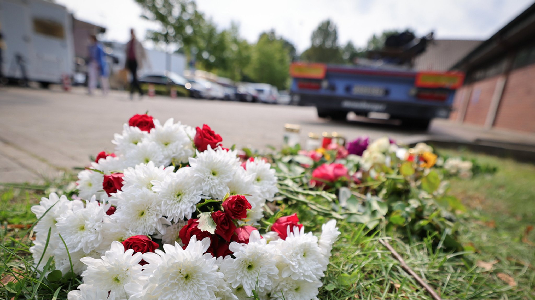 Zahlreiche Blumen und Kerzen sind nach einem tödlichen Radfahrerunfall mit einem abbiegenden Lkw auf einem Wiesenstück hinter dem von der Polizei gesicherten Lkw abgelegt.