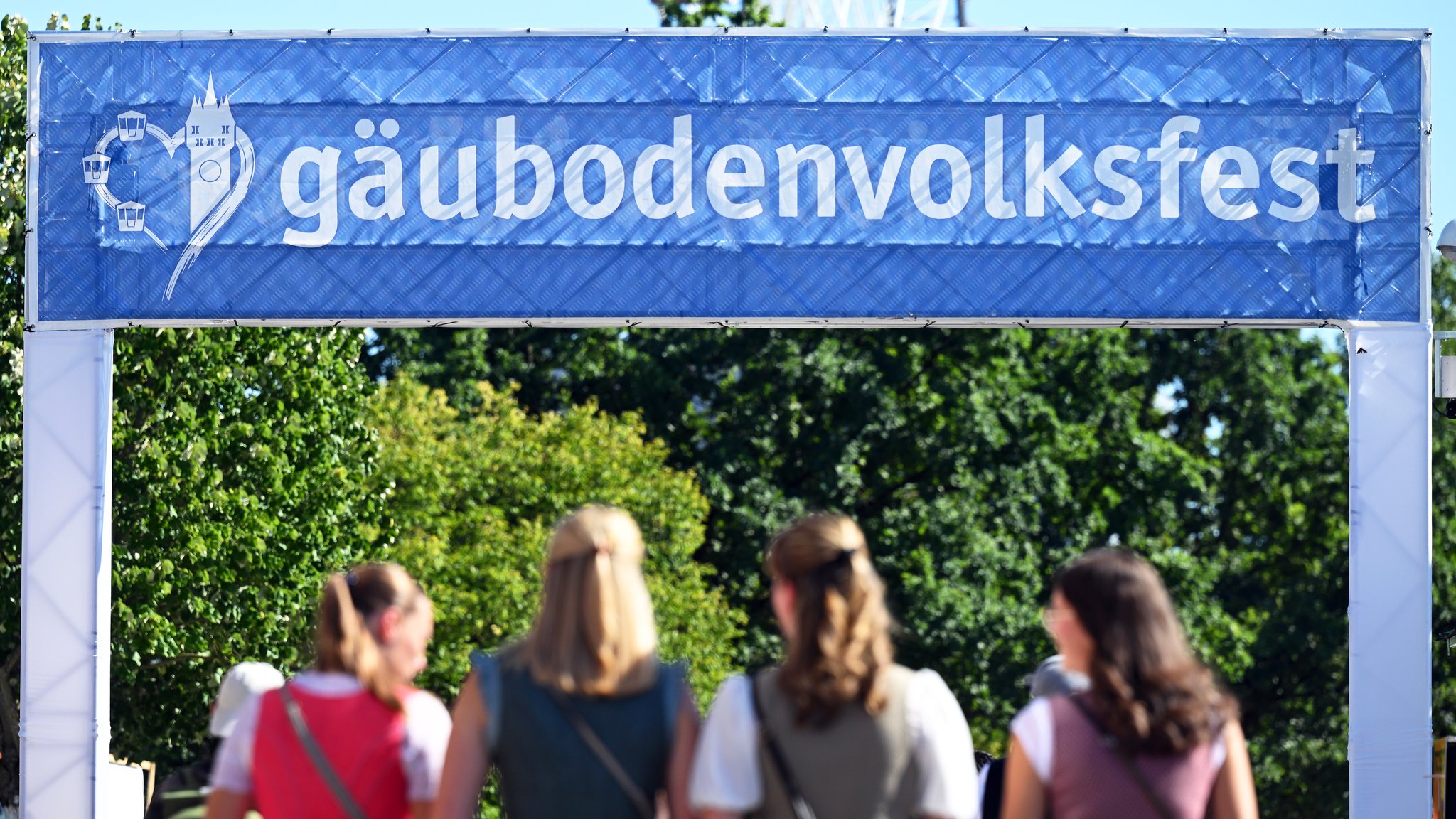 (Symbolbild) Junge Frauen im Dirndl laufen durch ein Tor, das mit "Gäubodenvolksfest" beschriftet ist. 
