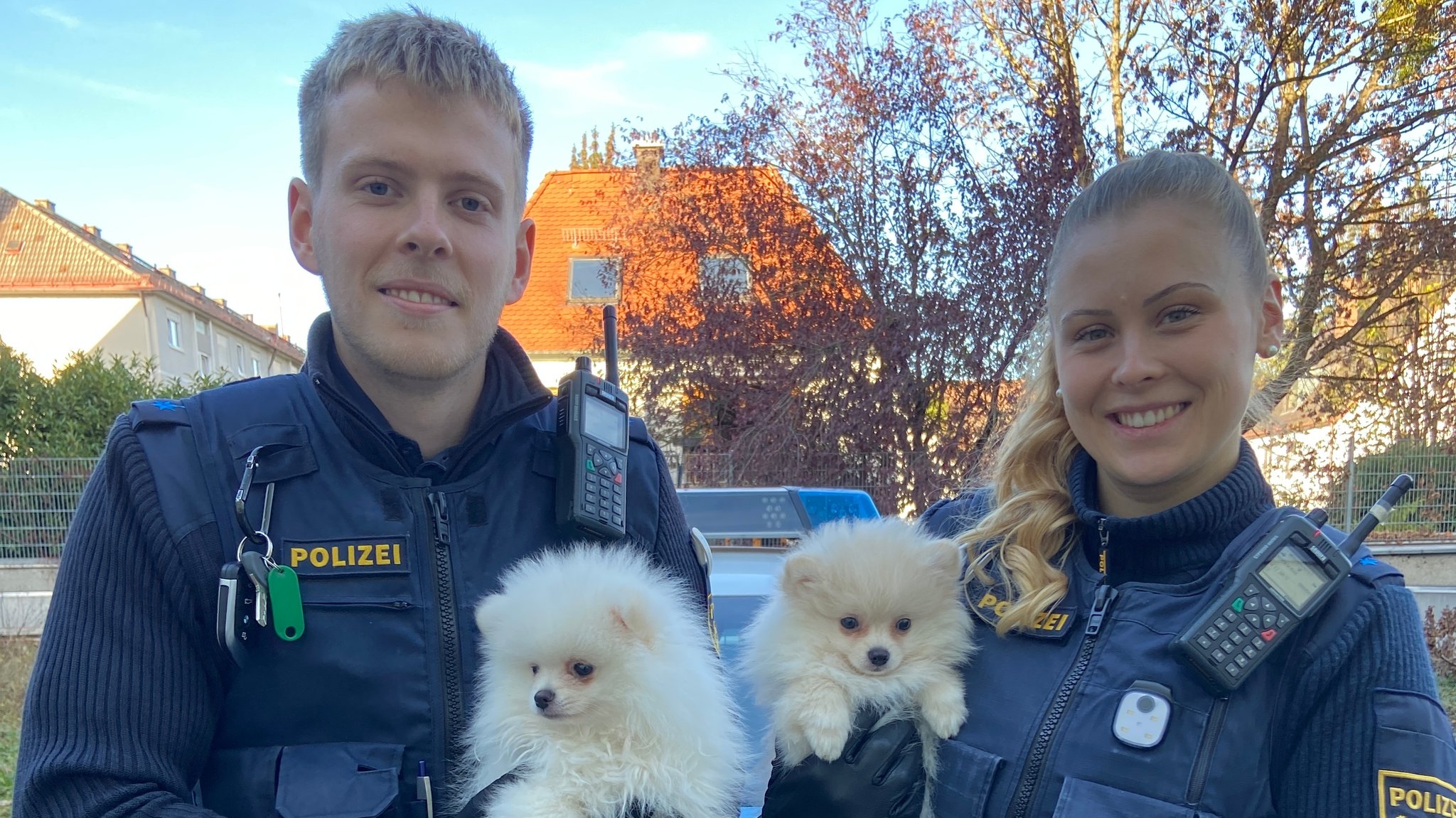 Ein Polizist und eine Polizistin mit zwei Welpen im Arm.