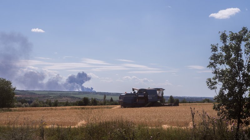 13.07.22: Getreidefeld in der ukrainischen Region Donezk, im Hintergrund steigt Rauch auf.