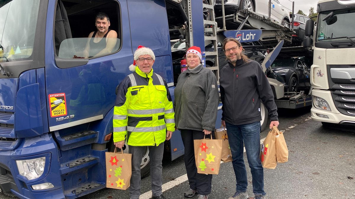 Drei Menschen mit Weihnachtstüten vor einem Autotransporter