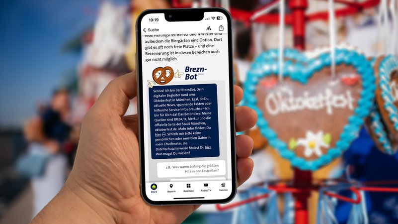 Jemand hält ein Handy in der Hand mit dem geöffneten BreznBot. Im Hintergrund ist unscharf ein Lebkuchenherz mit dem Schriftzug "Oktoberfest" zu sehen. | Bild: BR/Julia Knoblauch, Collage Wolfgang Zehentmeier Jemand hält ein Handy in der Hand mit dem geöffneten BreznBot. Im Hintergrund ist unscharf ein Lebkuchenherz mit dem Schriftzug "Oktoberfest" zu sehen.