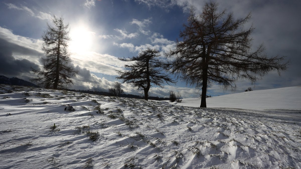 Die Sonne scheint durch eine Wolkenlücke über der mit Schneeverwehungen bedeckten Landschaft