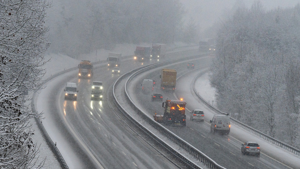Pkw, Lkw und ein Räumfahrzeug fahren bei winterlichen Verhältnissen auf einer Autobahn (Symbolbild)