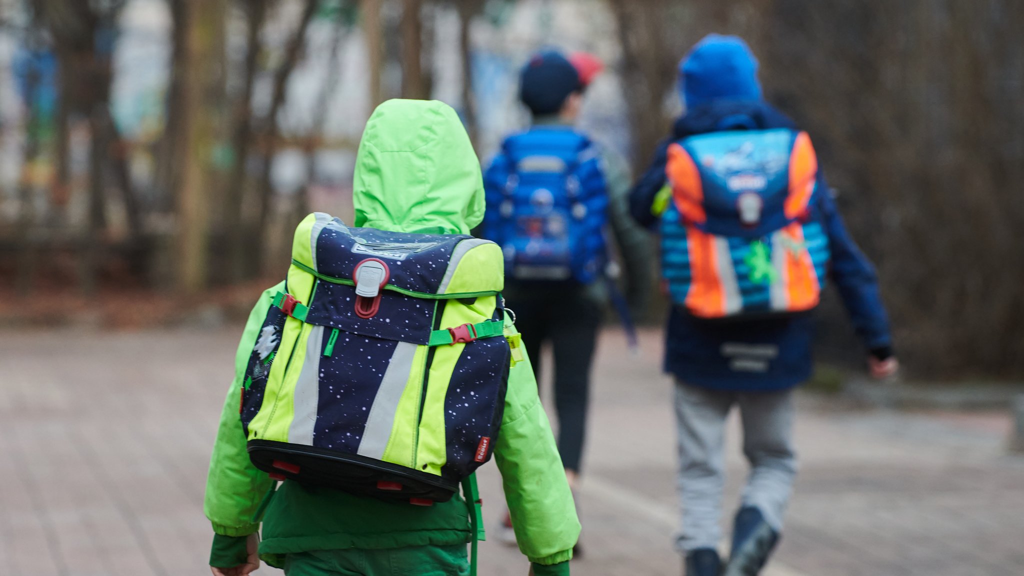 Drei Schüler gehen mit Schulranzen zum Eingang einer Grundschule