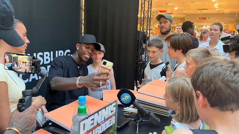 Basketballstar Dennis Schröder umzingelt von Fans in Regensburg. Hier hat er am Mittwoch (13.08.) sein neues Kinderbuch vorgestellt. | Bild: BR/Jasper Riemann Basketballstar Dennis Schröder umzingelt von Fans in Regensburg. Hier hat er am Mittwoch (13.08.) sein neues Kinderbuch vorgestellt.