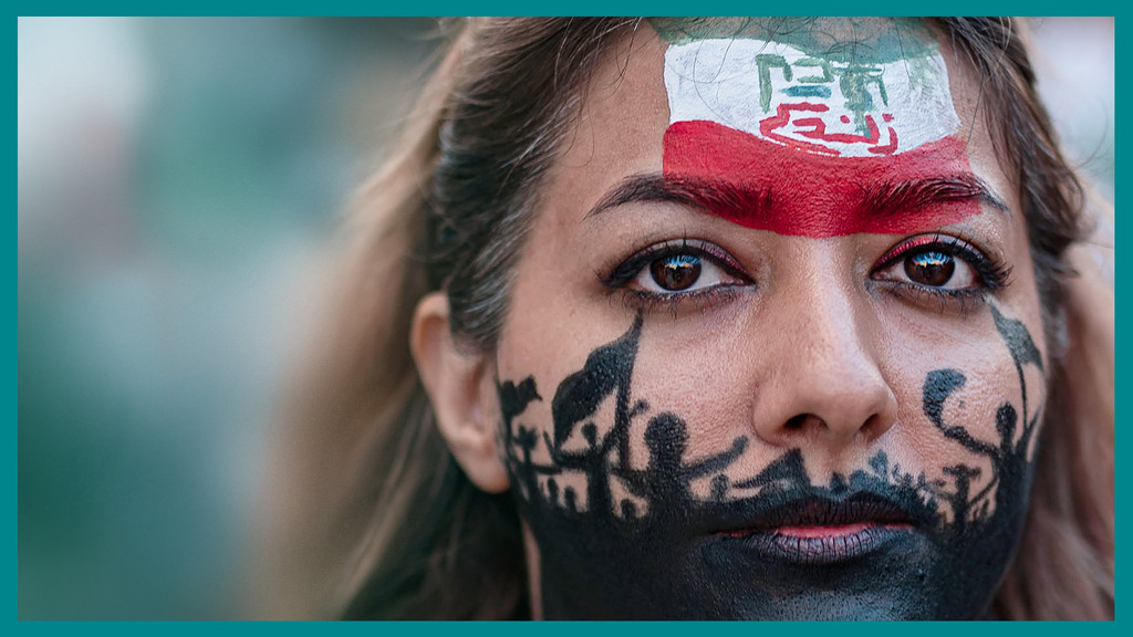 Stürzen Irans Frauen das Mullah-Regime? Im Bild: Demonstrantin aus Barcelona unterstützt die Iran-Proteste. Auf ihrer Stirn ist die iranische Flagge, um ihren Mund herum sind Schattenfiguren protestierender Menschen aufgemalt.