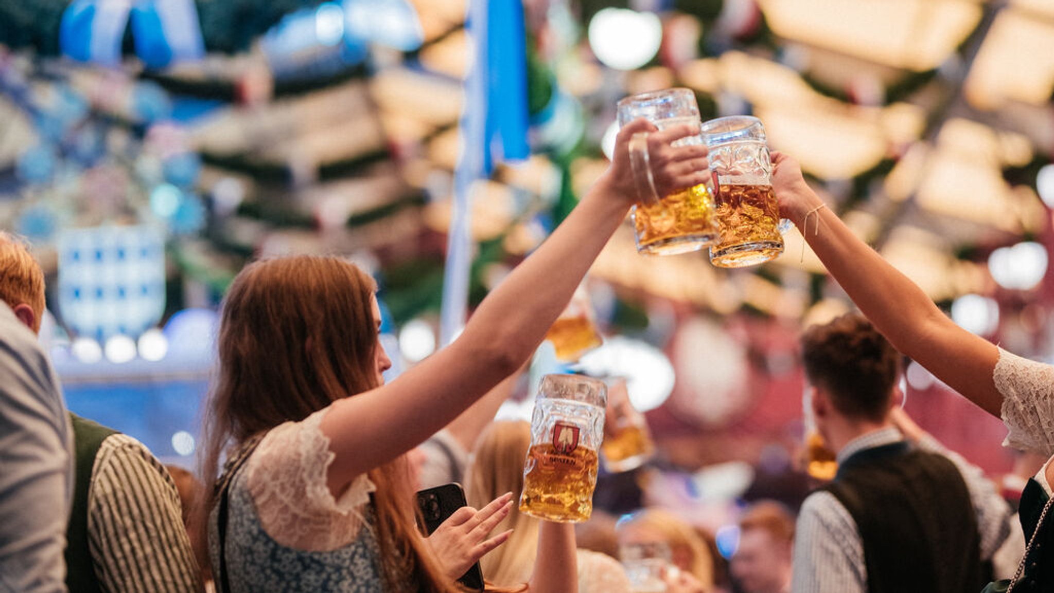 Zwei Frauen stoßen auf der Wiesn mit einer Maß an.