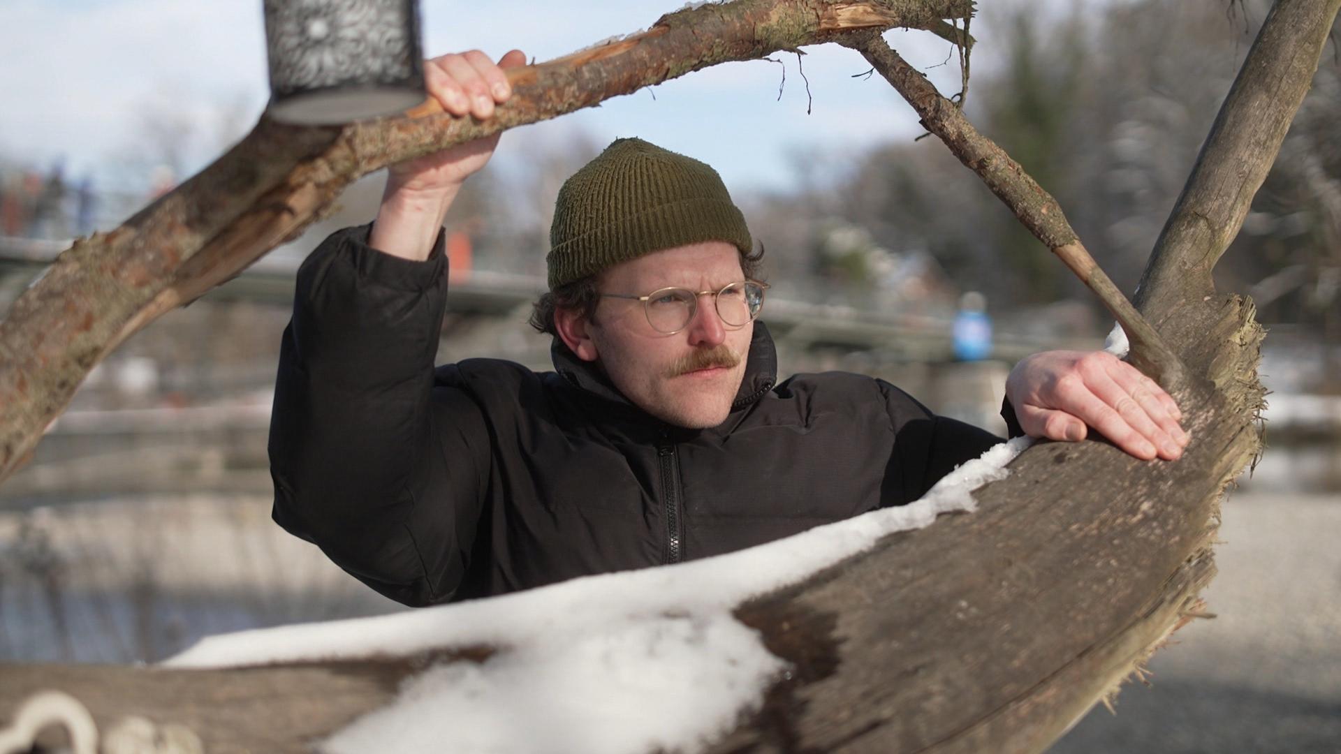 Ein Mann mit Mütze und Brille lugt zwischen zwei Ästen hervor