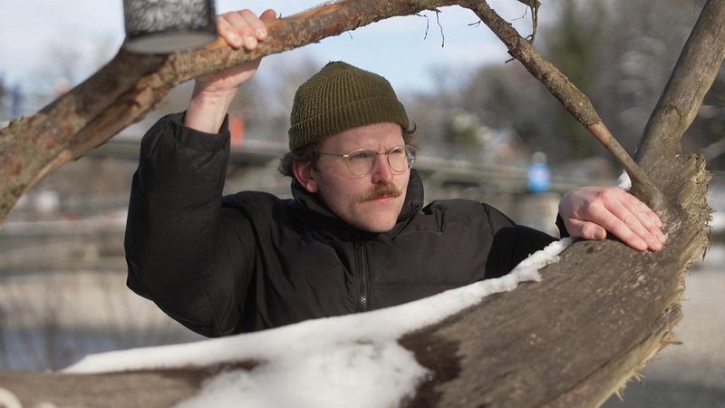 Ein Mann mit Mütze und Brille lugt zwischen zwei Ästen hervor | Bild: BR Ein Mann mit Mütze und Brille lugt zwischen zwei Ästen hervor
