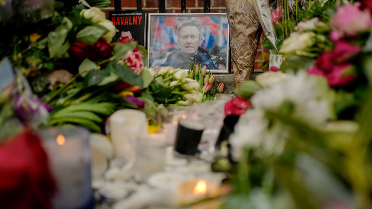 17.02.2024, Großbritannien, London: Ein Porträt von Alexej Nawalny ist zwischen Blumen und Kerzen vor der russischen Botschaft in London zu sehen.