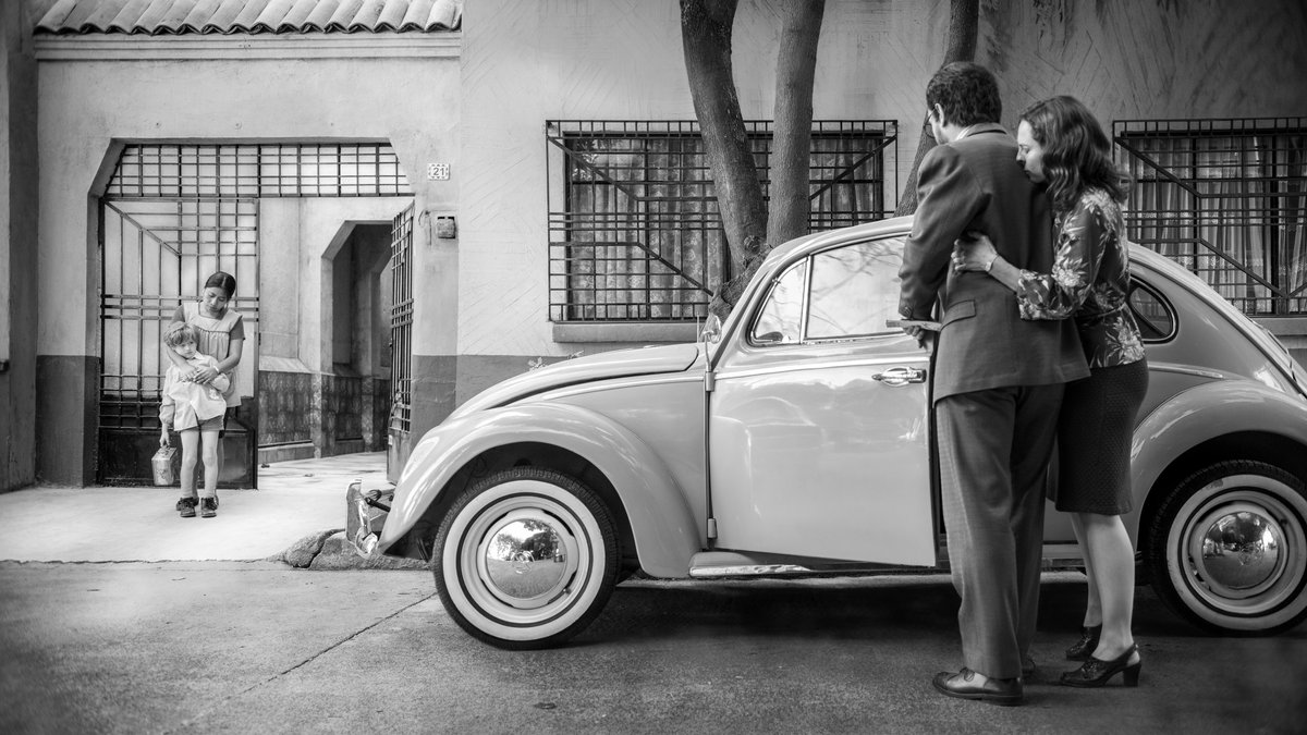 Filmszene aus "Roma": Ein Paar neben einem VW-Käfer vor einem Haus, Kindermädchen und Kind stehen vor dem Hoftor.